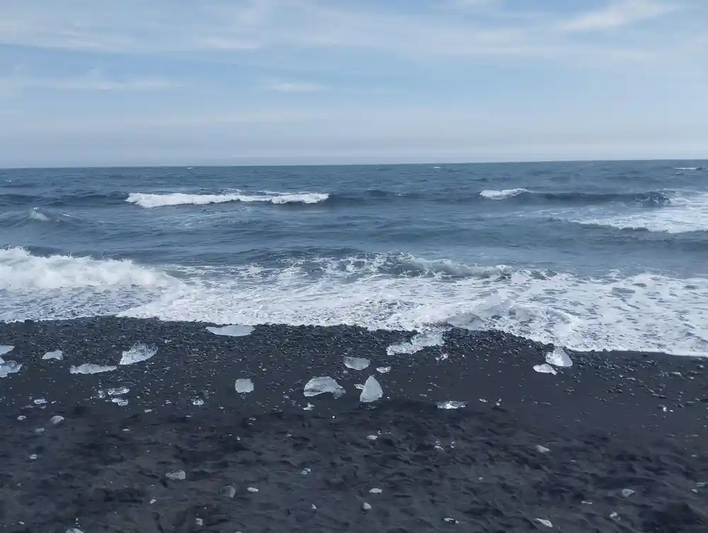 Black sand beach with white ice chunks and waves