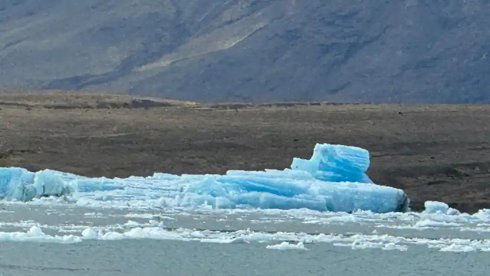 Blue ice chunks on dark sand beach with mountains