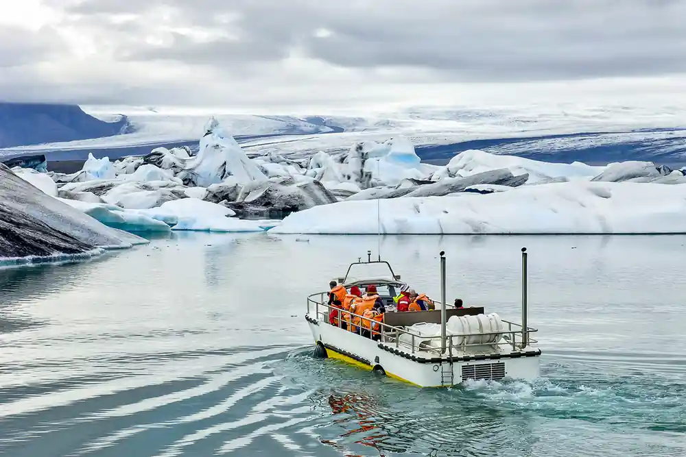 Boat with passengers near white icebergs and glacier lagoon