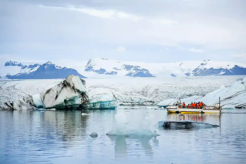 Boat near turquoise icebergs and white glacier with mountains
