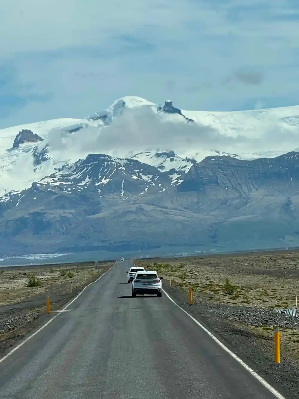 Car driving on road toward snow-capped volcano mountain