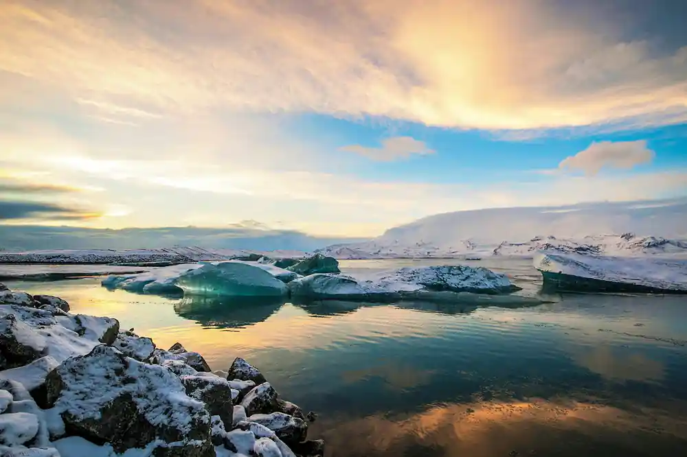 Green icebergs in calm water with snowy mountains