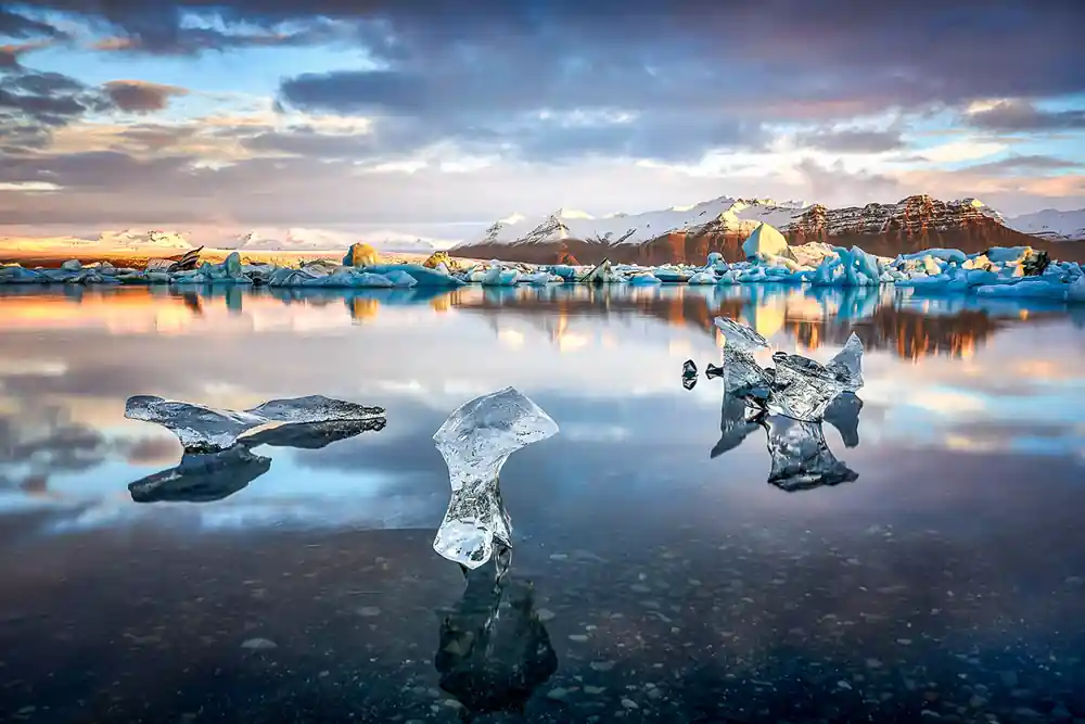 Icebergs reflected in shallow lagoon at sunset