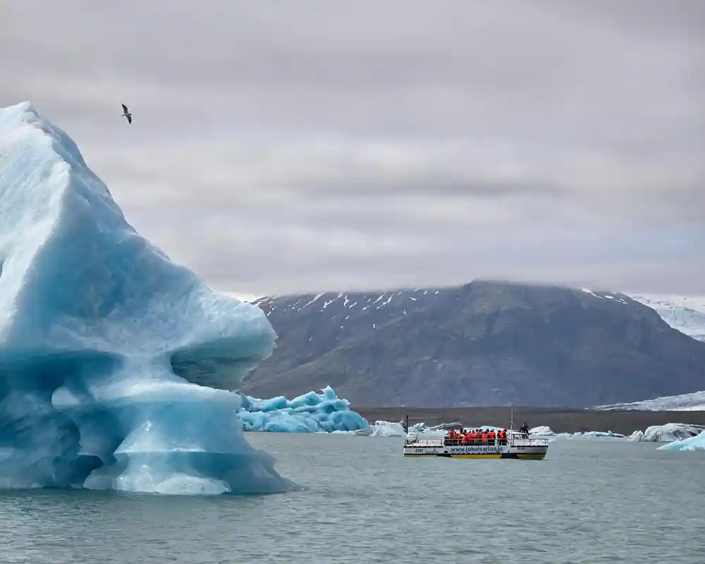 Large blue iceberg with boat and mountain in distance