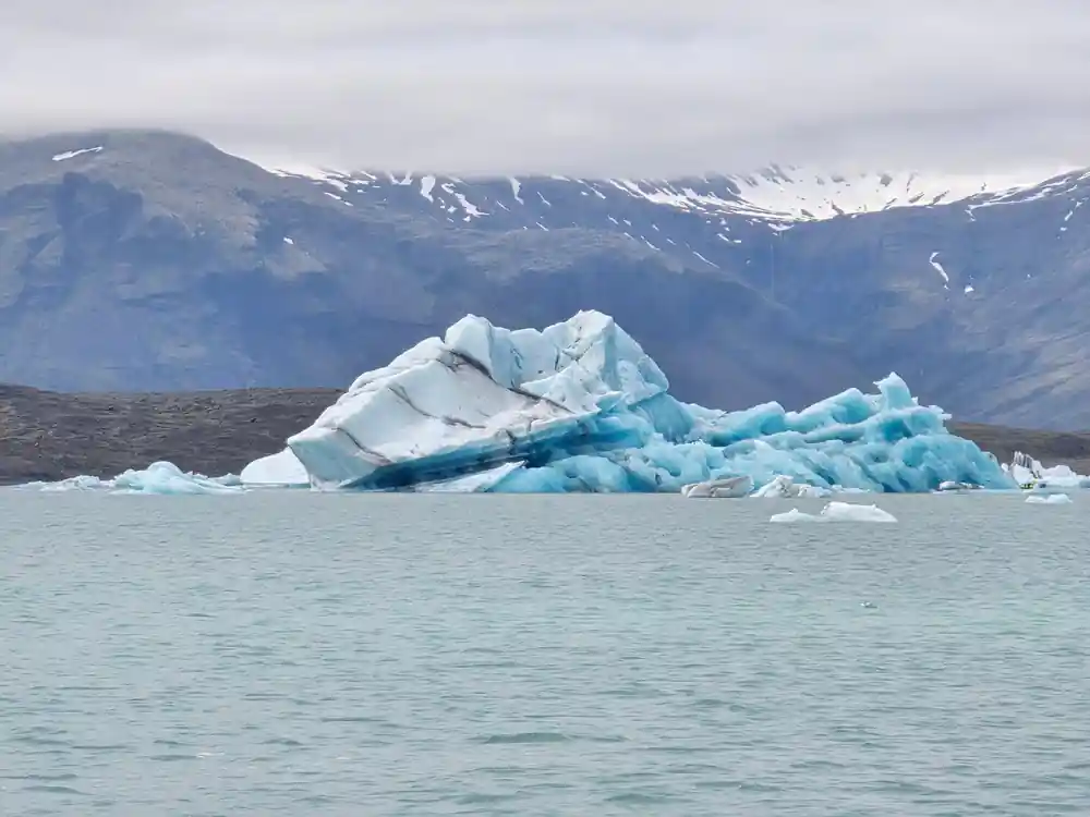 Large turquoise iceberg floating in glacial lake with mountains