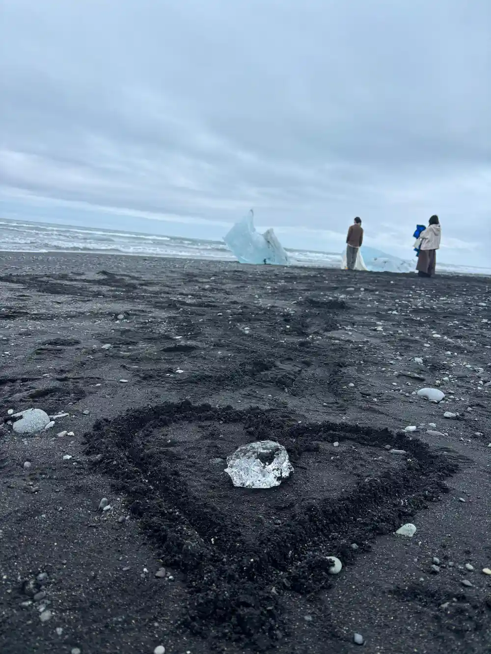 People standing on black sand beach near iceberg