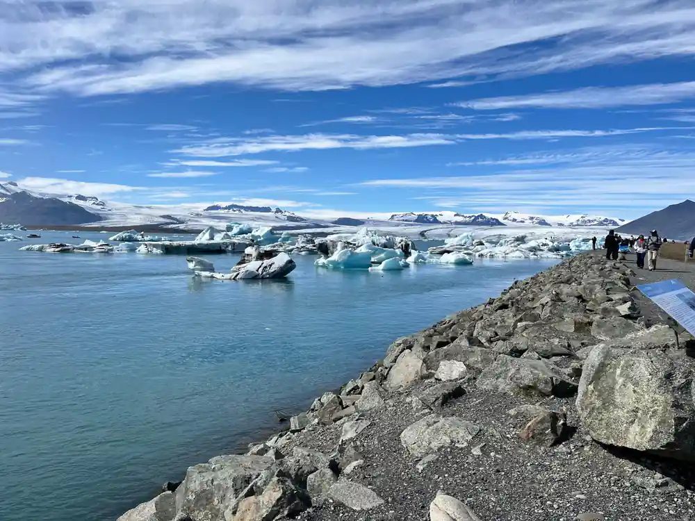 People standing on rocky shore viewing glacier and icebergs