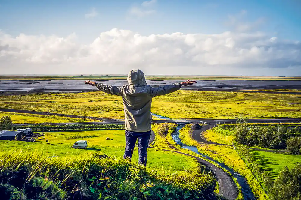 Person with arms raised in vast green valley