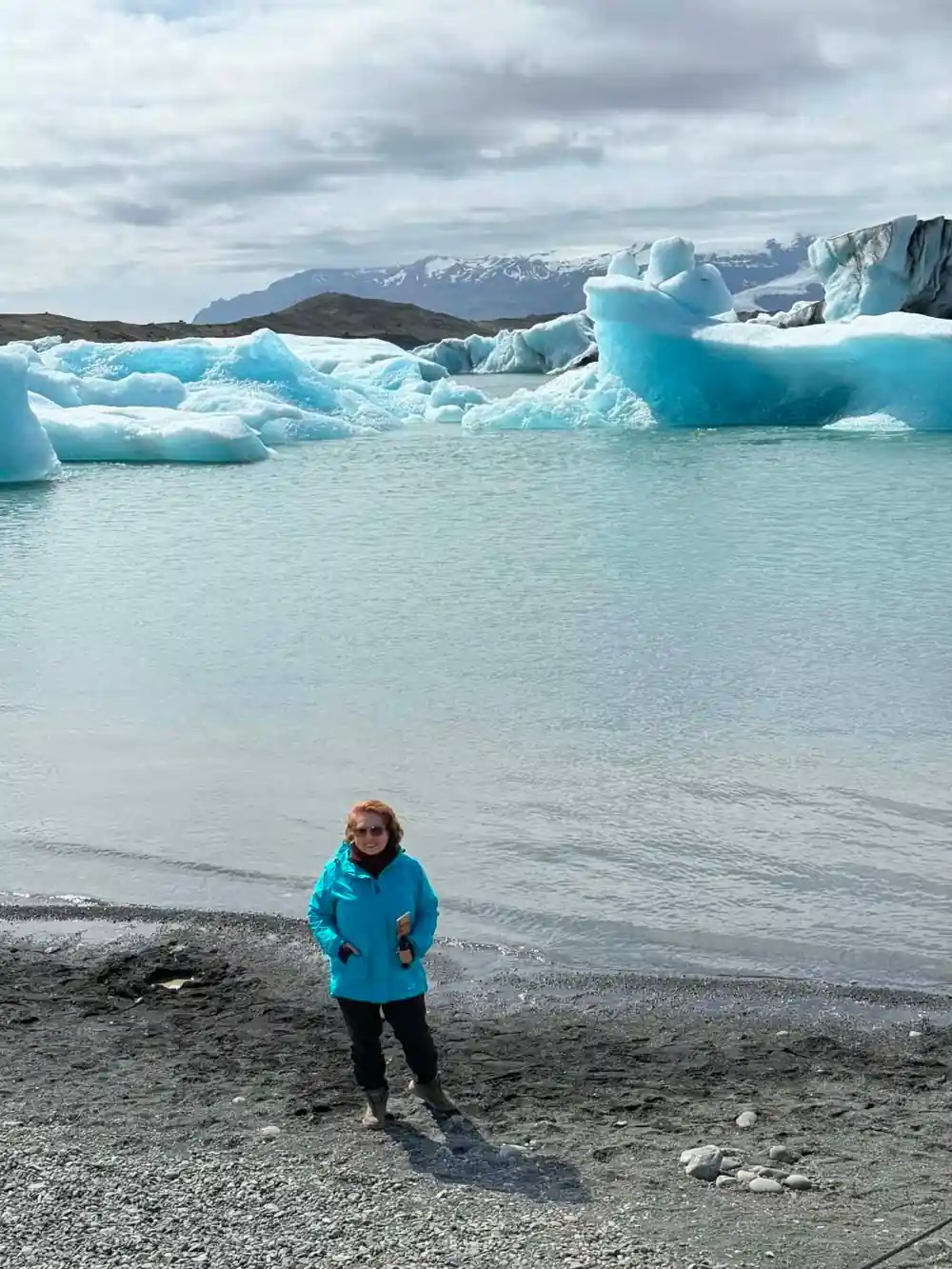 Person in blue jacket standing on beach with icebergs