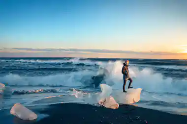 Person standing on beach with waves and ice chunks