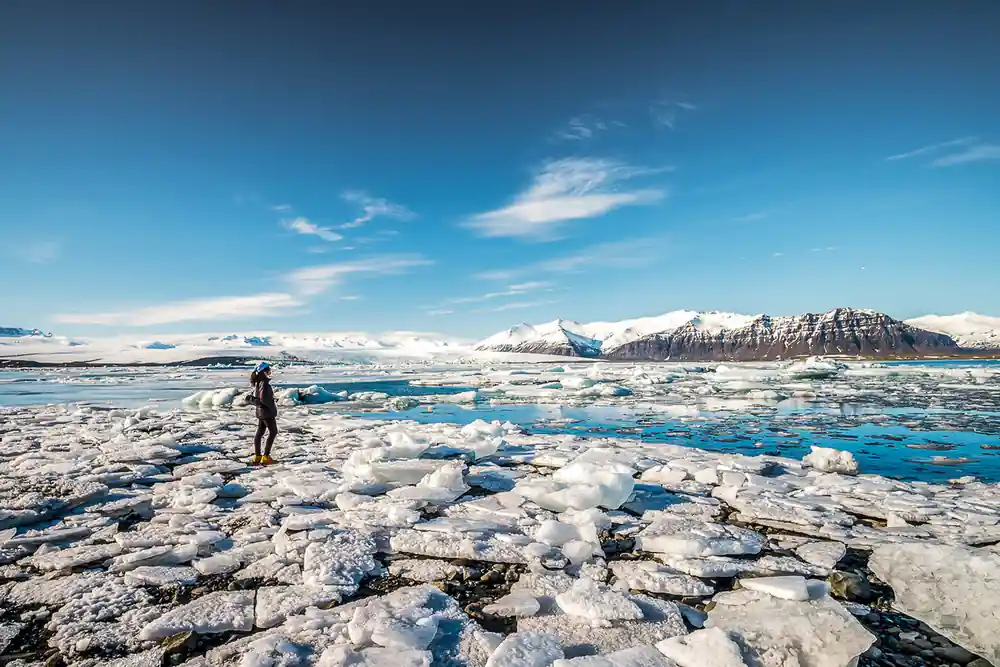 Person standing on ice with blue icebergs and clear sky
