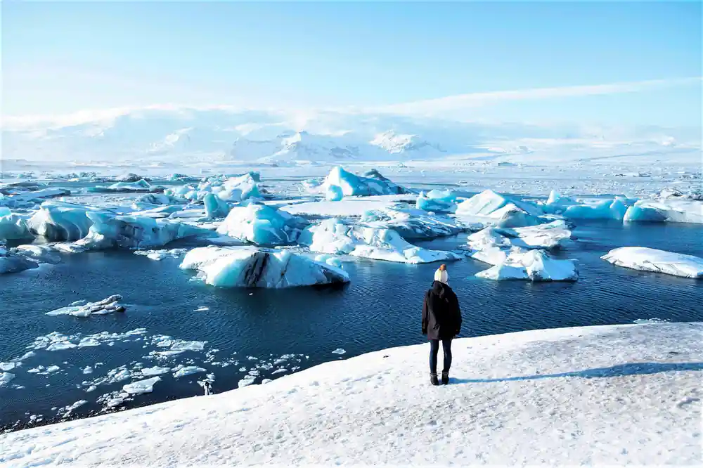Person standing on ice field with icebergs and mountains