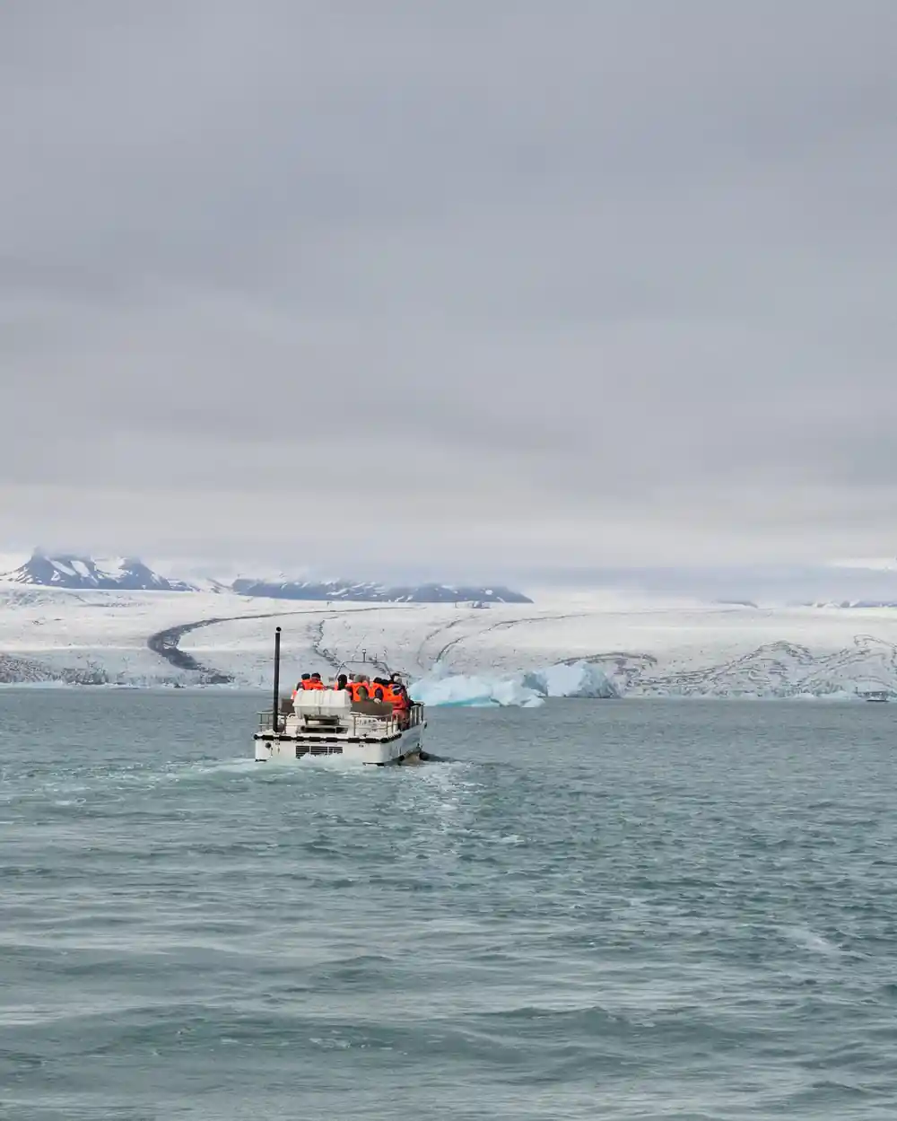 Small boat with passengers near icebergs and snowy mountains