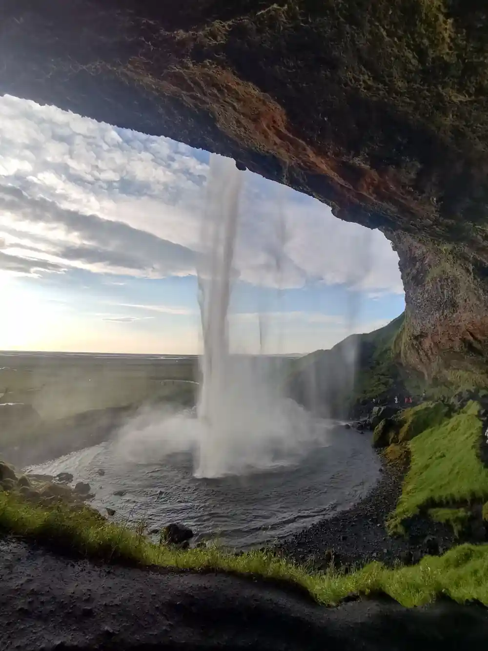 Waterfall cascading from cave beneath overhanging cliff