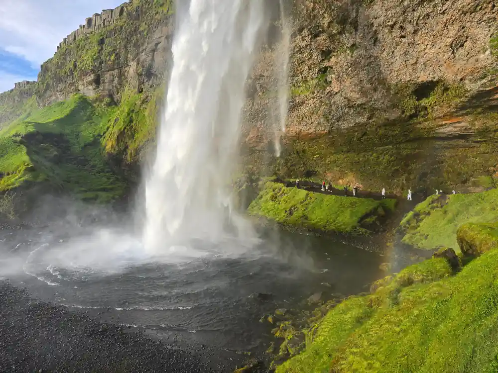 Waterfall cascading from moss-covered cliff with people viewing