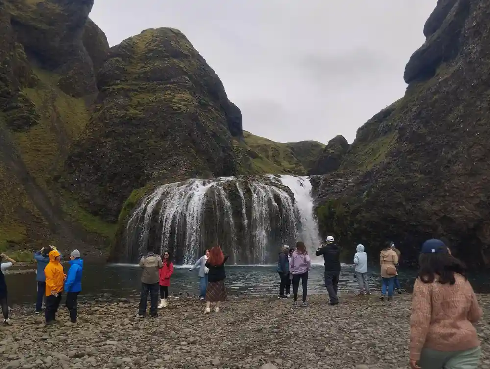Waterfall between moss-covered cliffs with tourists watching