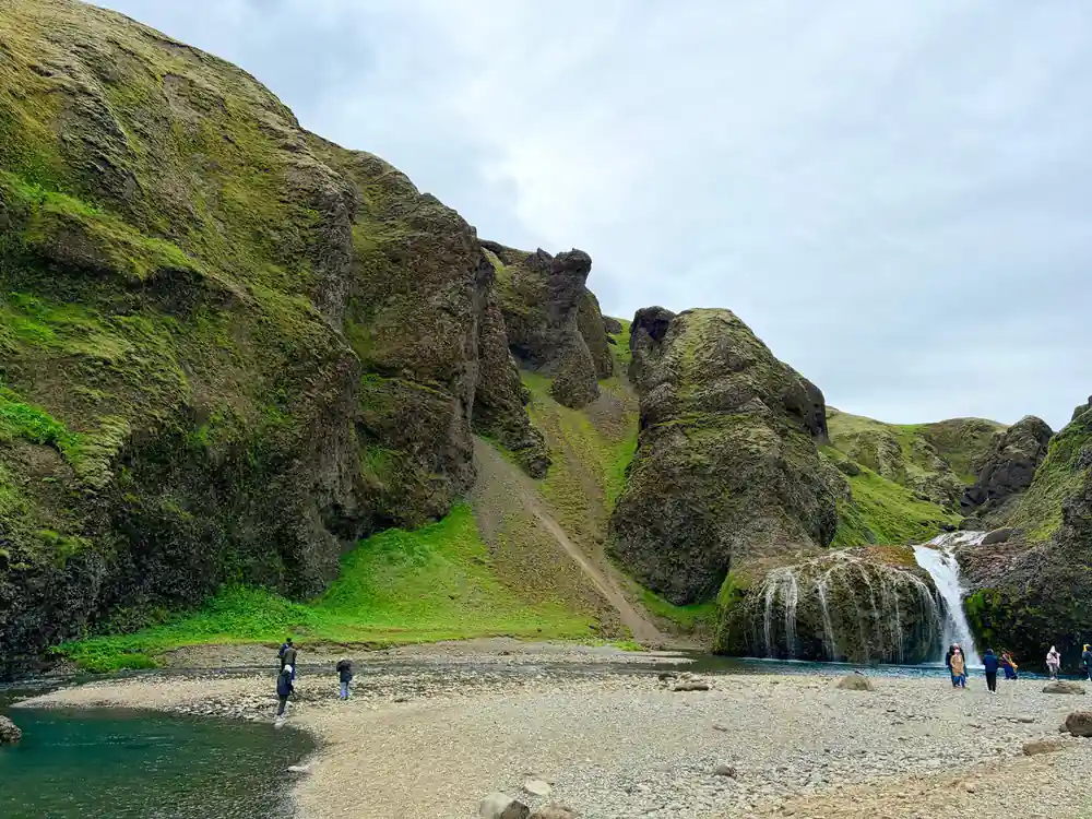 Waterfall in steep canyon with tourists on beach below