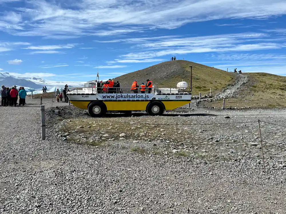 Yellow amphibious vehicle with tourists on gravel plain